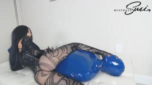 Woman in fishnet stockings and leather outfit lying on a bed with a blue mask.